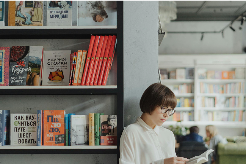 Woman standing in a bookshop leaning against wall and reading.